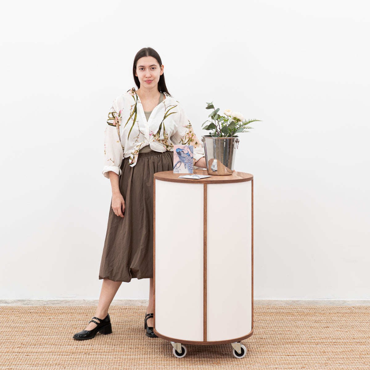 Biały okrągły stojak dla gospodarzy z dużą ilością półek i eleganckim wyglądem, idealny do profesjonalnych ekspozycji w sklepach typu pop-up i przestrzeniach eventowych.