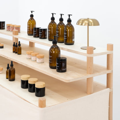 Detail of display shelves on a wooden check stand with skincare bottles and minimalist lamp