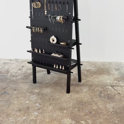 Product video showcasing the foldable A-frame pegboard display stand with peg hooks, rear shelving, and logo panel in matte black